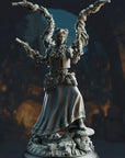 A detailed 3D rendering of a female character with multiple arms, wearing a long skirt and holding various weapons, standing in a dark, cave-like setting.