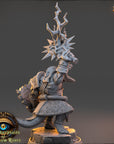 A 3D rendering of a fantasy character, possibly a warrior or magical being, with a large headdress or crown and various weapons or armor. The character appears to be standing on a rock formation or pedestal, with a dark background.